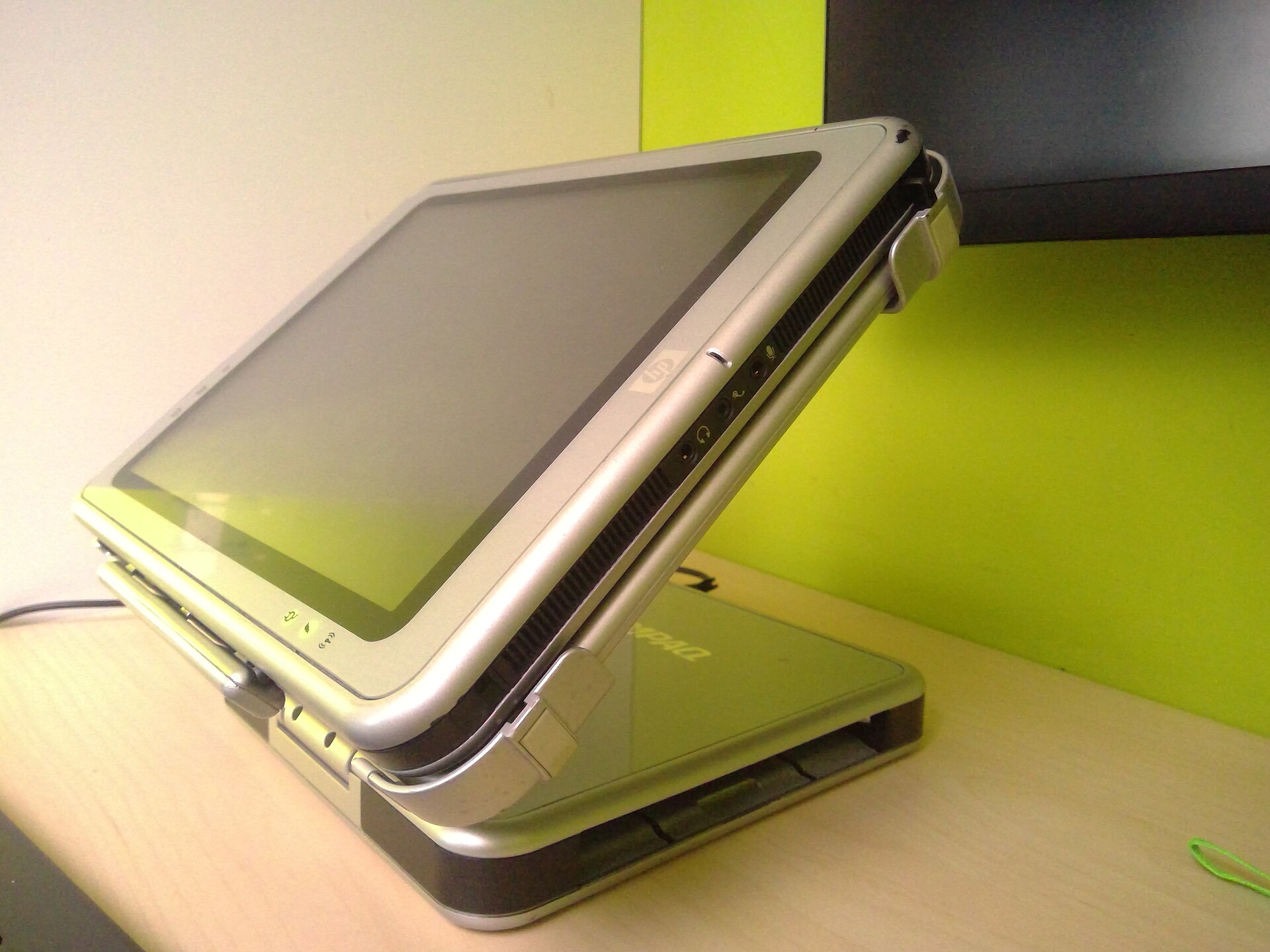A HP TC1100, which is a tablet from 2004 running Windows XP Tablet PC Edition, is currently being docked in its docking station, which allows an user to easily connect their tablet to charge, output video to a secondary VGA monitor, use wired Ethernet, connect devices to 4 USB ports and provides audio input and output.