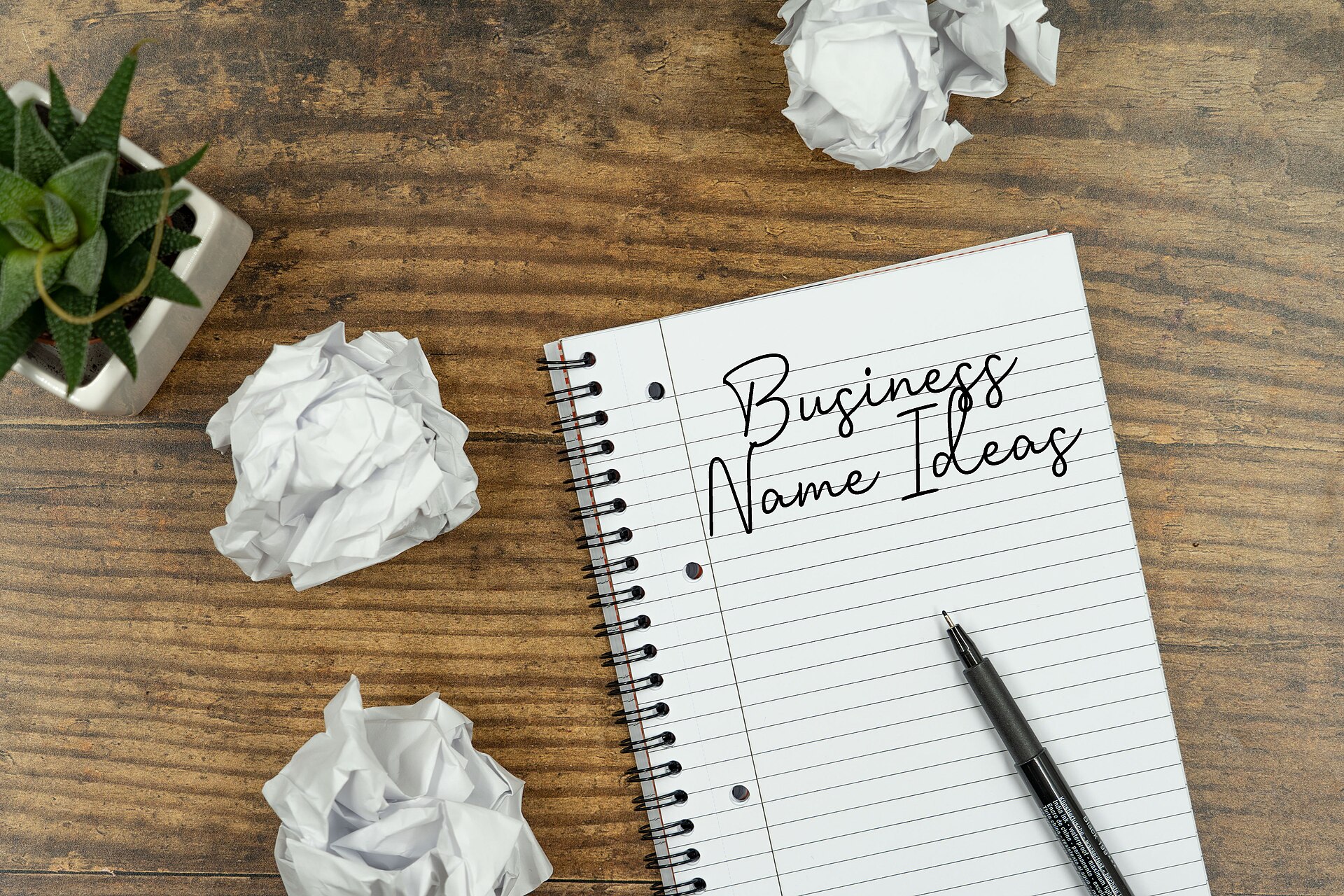 A photo of a note book with 'business name ideas' written on it and several scrunched up papers scattered around. This image is 100% free to use when you provide creidt by linking back to:https://customneon.co.uk/