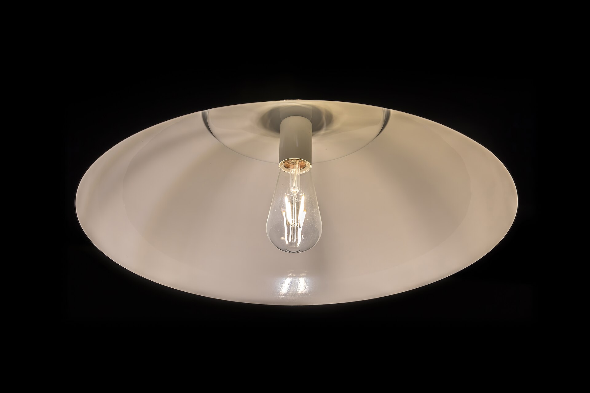Lampshade on the ceiling with lit incandescent light bulb, and a black background.
